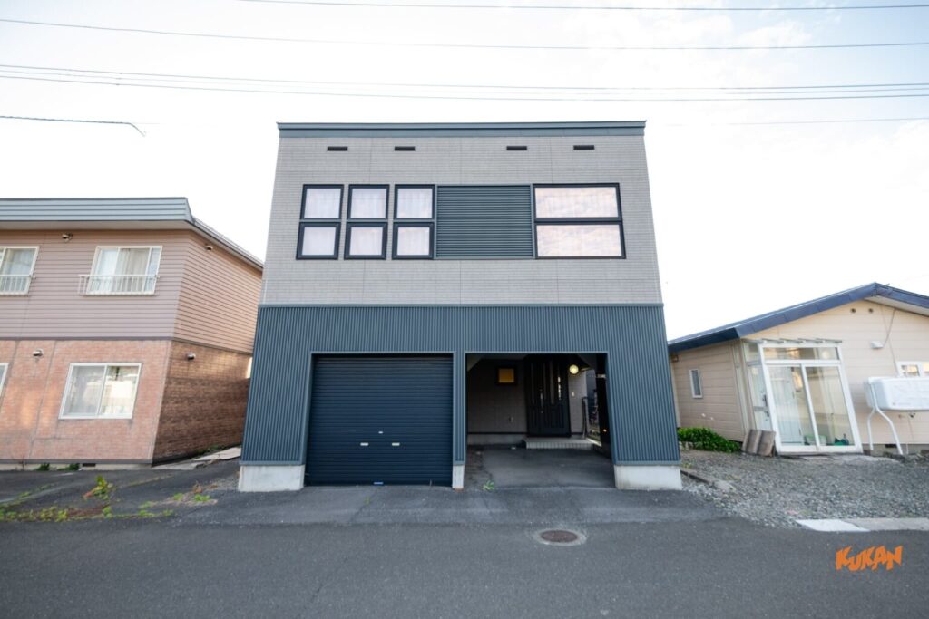 上富良野の社員寮や宿舎に適した大型中古戸建て物件の、シャッター付き車庫と玄関がある正面外観