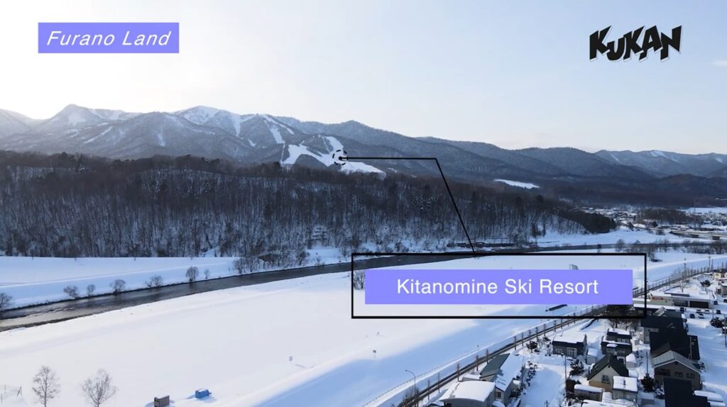 冬の雪に包まれた北海道富良野市の空撮写真。遠景に「Kitanomine Ski Resort」と指し示されたスキー場と雪山連峰が広がる。「Furano Land」のテキスト、右上に「KUKAN」のロゴ。