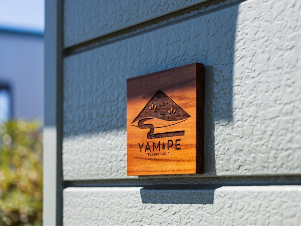 富良野の一棟貸し民泊『YAM-PE』の外壁に取り付けられた木製ロゴ看板